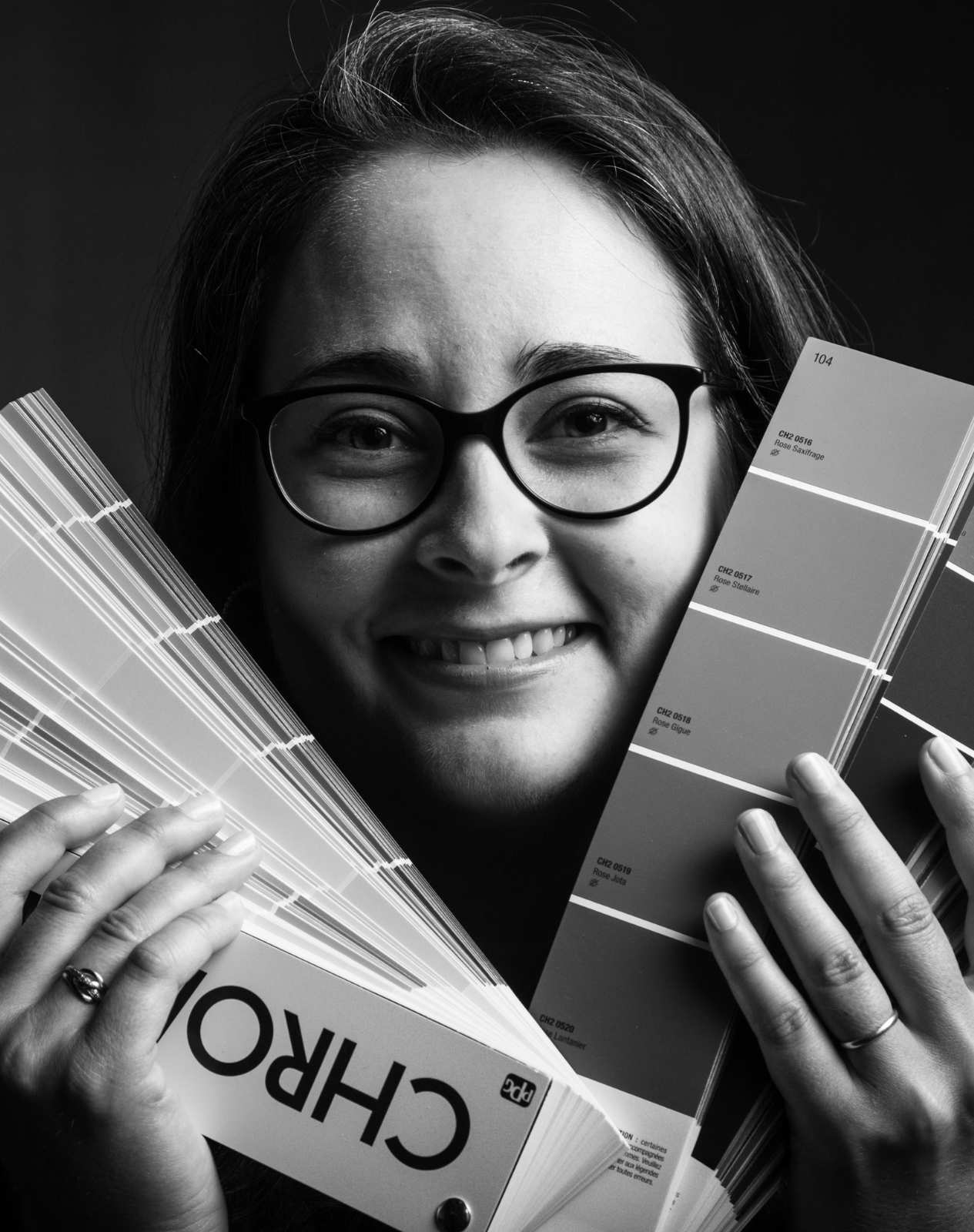 portrait en noir et blanc de Delphine Déco Rennes avec un nuancier à la main et un large sourire, prête à travailler sur vos projet de décoration et d'aménagement d'intérieur, spécialiste de l'ergonomie de l'habitat