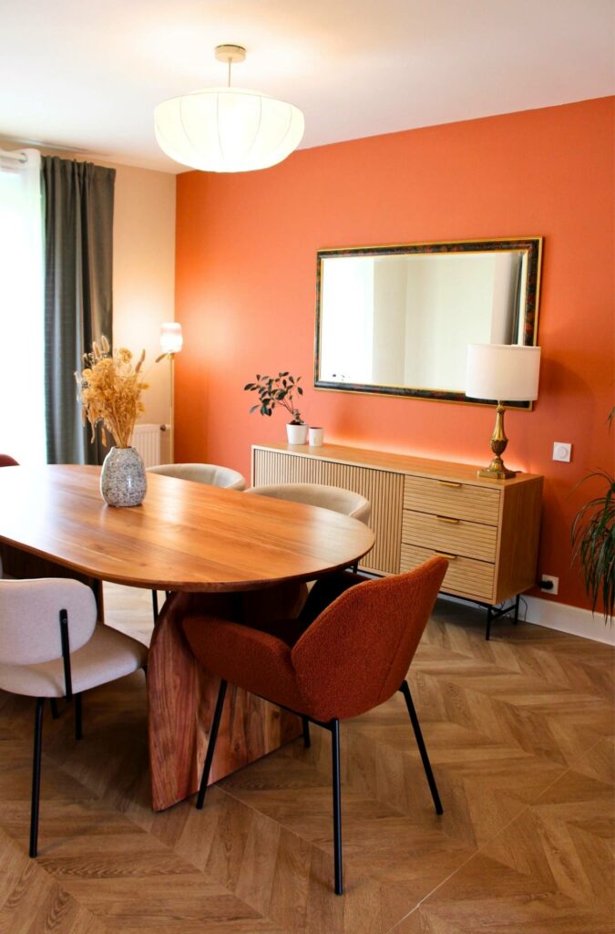 Une salle à manger très conviviale et chaleureuse avec un mur couleur terracotta, un buffet en bois, une table ovale en bois brut et des chaises en tissu bouclette