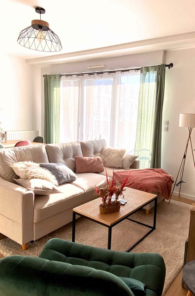 Un séjour plein de douceur avec un canapé beige en velours côtelé, un fauteuil vert sapin et des accessoires rose poudrés. 